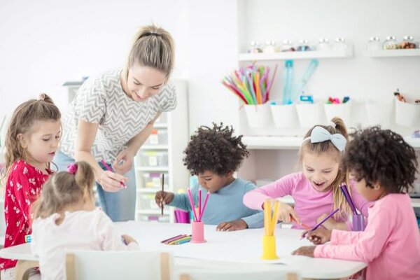 Kindergartenkinder malen zusammen mit einer jungen Frau am Tisch – 